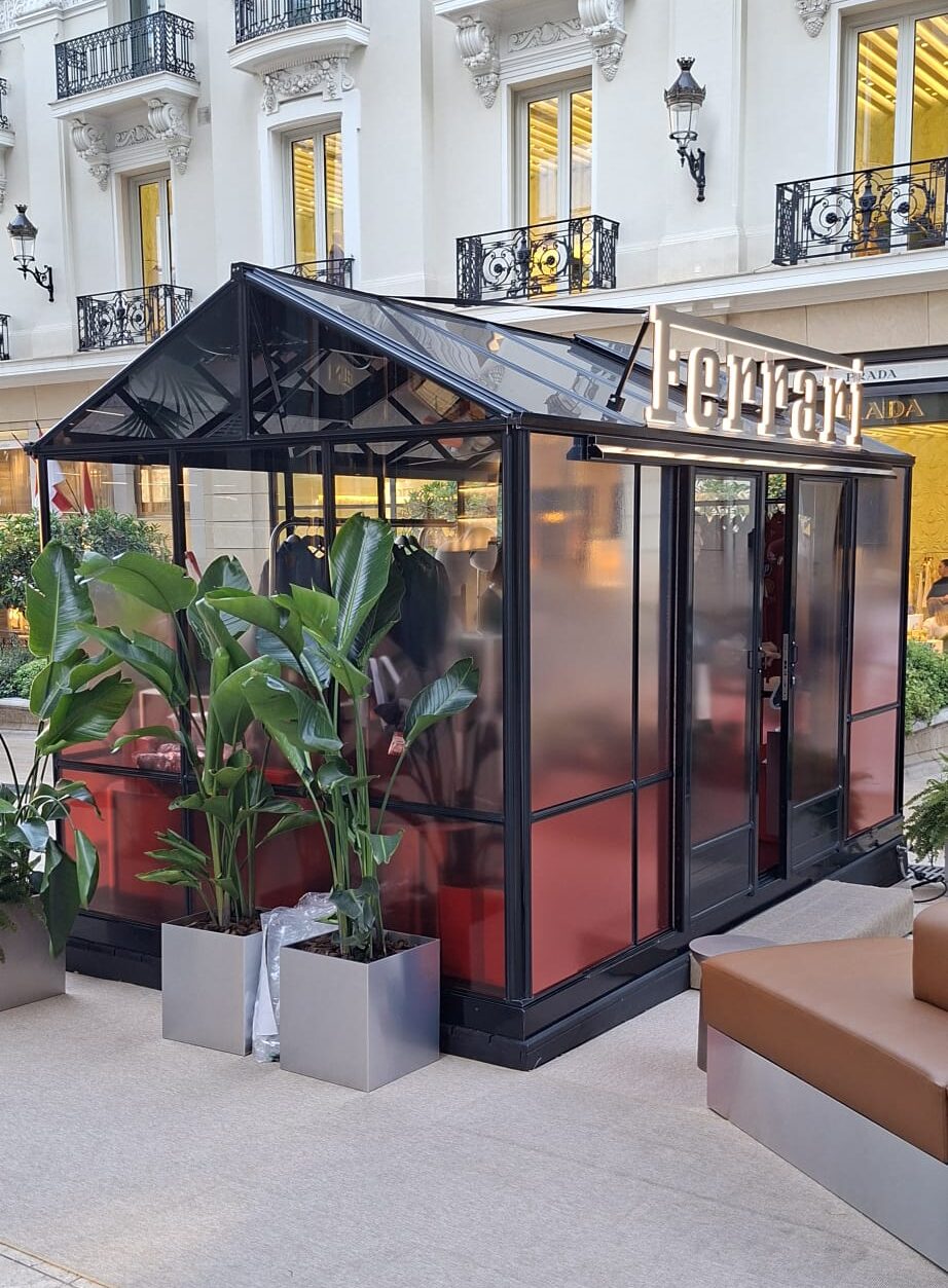 Posa di pellicole satinate sfumate sui vetri perimetrali della glass house Ferrari a Monaco, con focus sulla facciata d'ingresso, l'insegna del brand e le installazioni di verde per il visual merchandising.