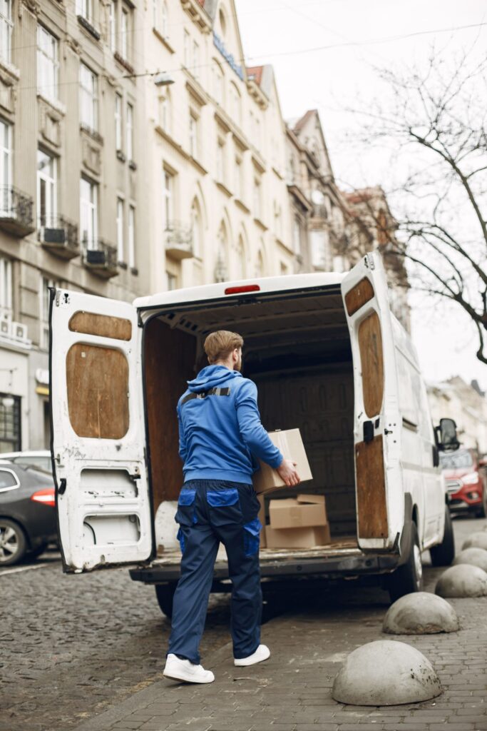 Home 11 Operator loading boxes into a delivery van on a city street for a retail relocation service.