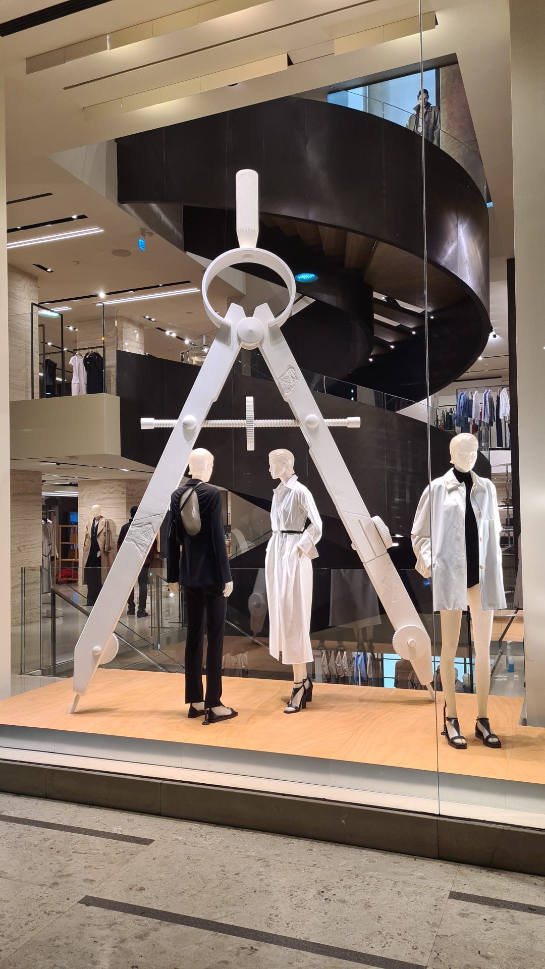 Installazione artistica con un grande compasso geometrico bianco su misura e pedana in legno per il flagship store Max Mara a Milano.